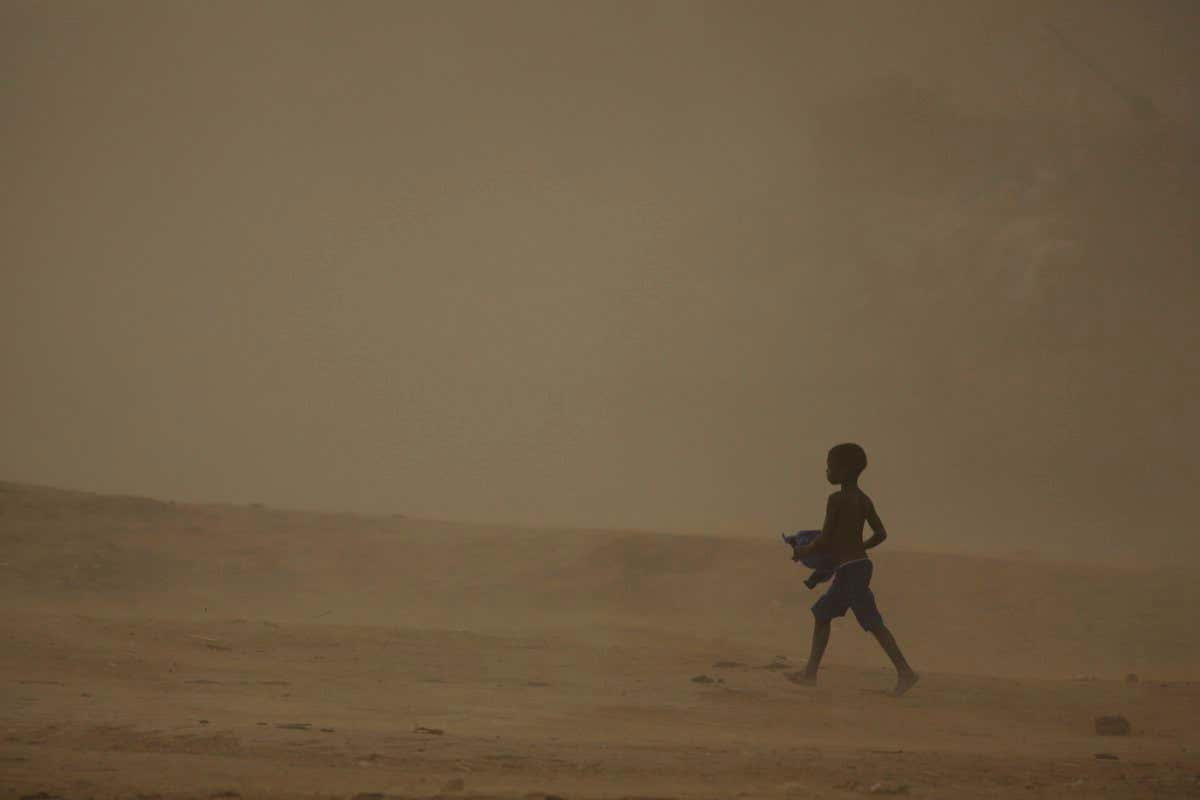 A young boy walks across dusty arid desert land at sunset. Location: Djenne ( Djenn?? ), Mopti, Mali, Africa