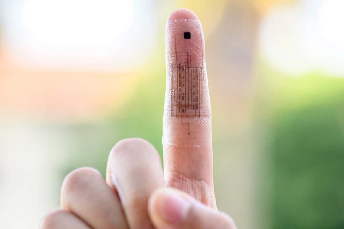 An outstretched pointer finger has a translucent skin wrapped around it. This electronic skin shows black sensors and circuitry embedded within.