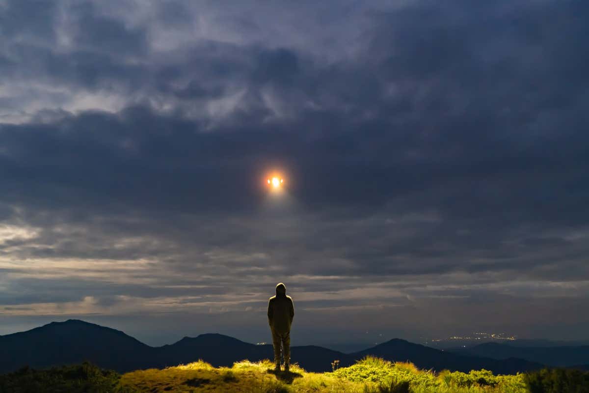 The UFO shines on a male standing on the mountain; Shutterstock ID 1476587882; purchase_order: -; job: -; client: -; other: -