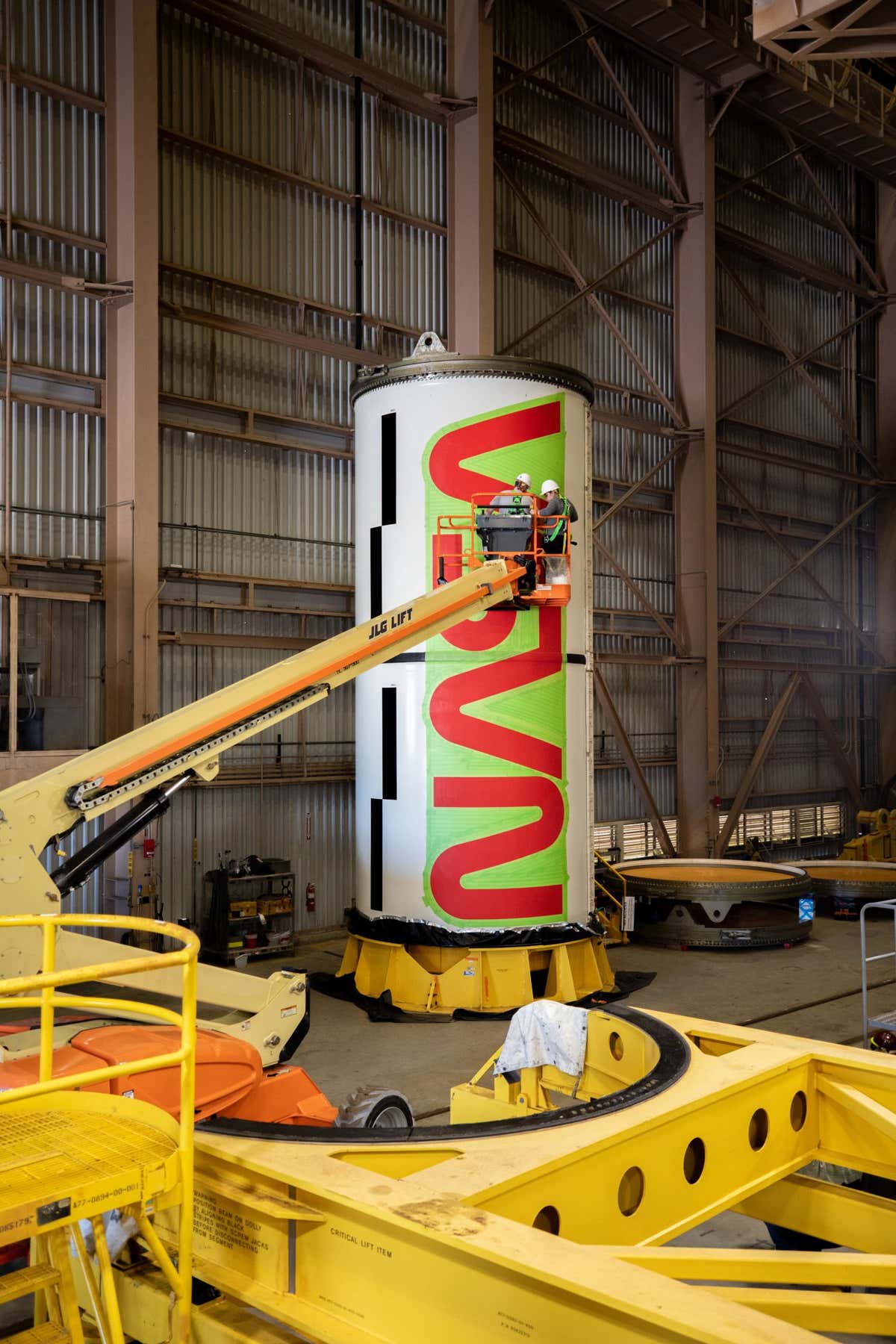 Workers with NASA???s Exploration Ground Systems (EGS) paint the bright red NASA ???worm??? logo on the side of an Artemis II solid rocket booster segment inside the Rotation, Processing and Surge Facility (RPSF) at Kennedy Space Center in Florida on Tuesday, Jan. 30, 2024. The EGS team used a laser projector to mask off the logo with tape, then painted the first coat of the iconic design. The booster segments will help propel the Space Launch System (SLS) rocket on the Artemis II mission to send four astronauts around the Moon as part of the agency???s effort to establish a long-term science and exploration presence at the Moon, and eventually Mars.