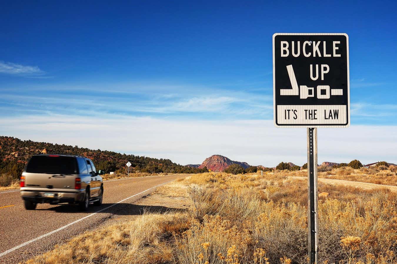 A car passes a "Buckle Up It's The Law" sign along an Arizona highway