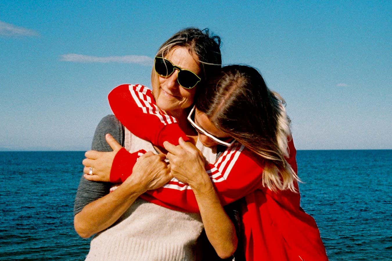 Woman hugging her mother in front of sea under sky