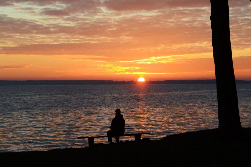 REMFH5 Landscape with silhouette of a person sitting on a bench, sunset and altocumulus clouds over the sea..