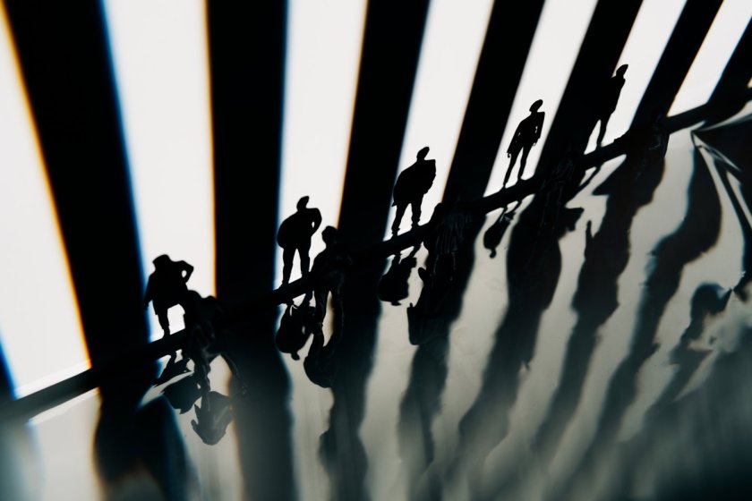 A group of small silhouetted figures stands along a sharp edge against a backdrop of bright vertical stripes of light.